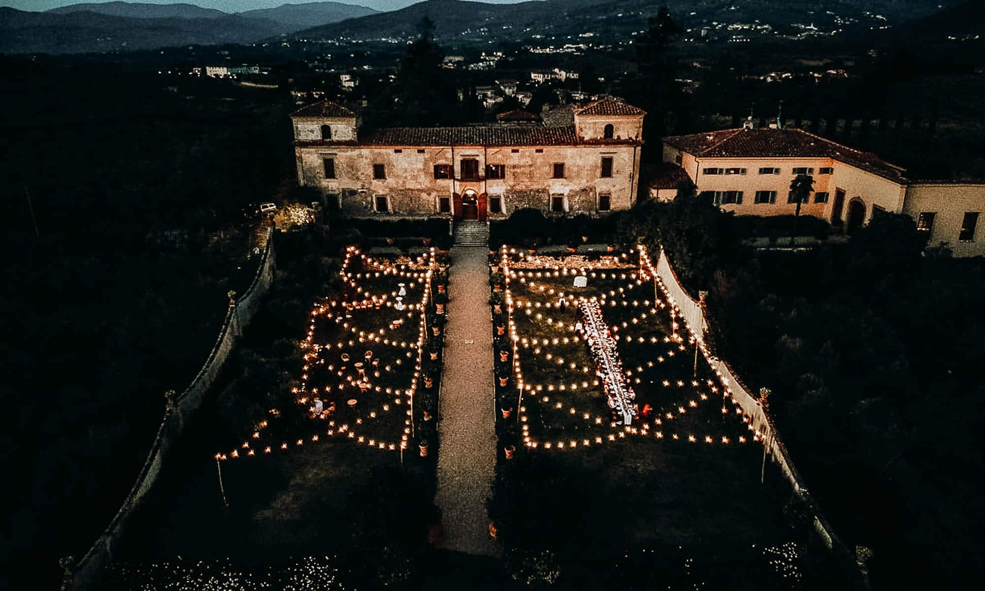 Aerial view of a Tuscany wedding venue featuring a garden illuminated with lights at night.