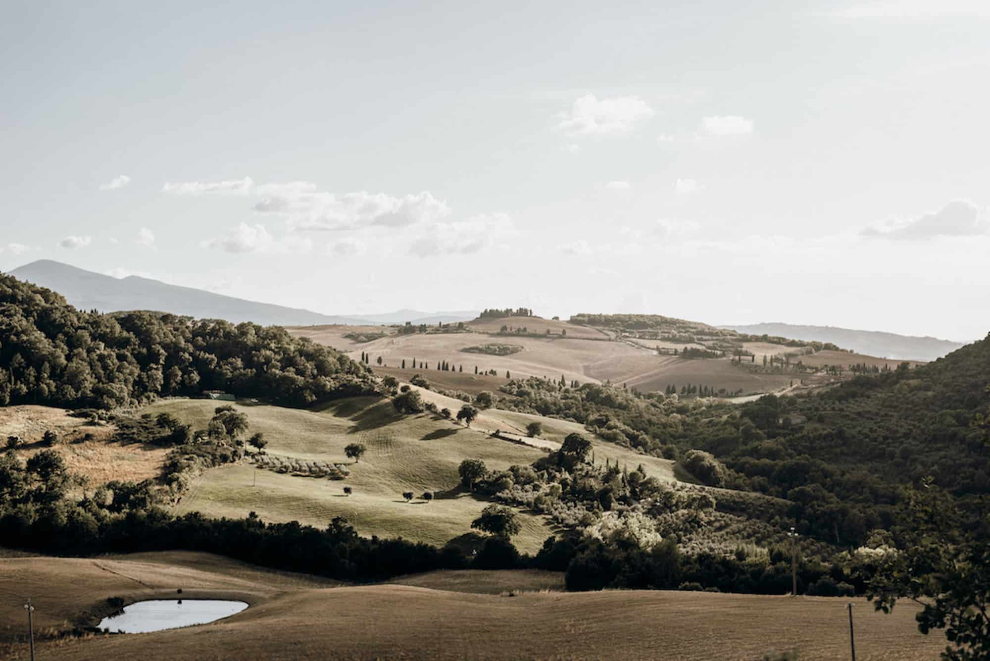 Scenic view of rolling hills and trees in the Tuscany region under a clear sky.