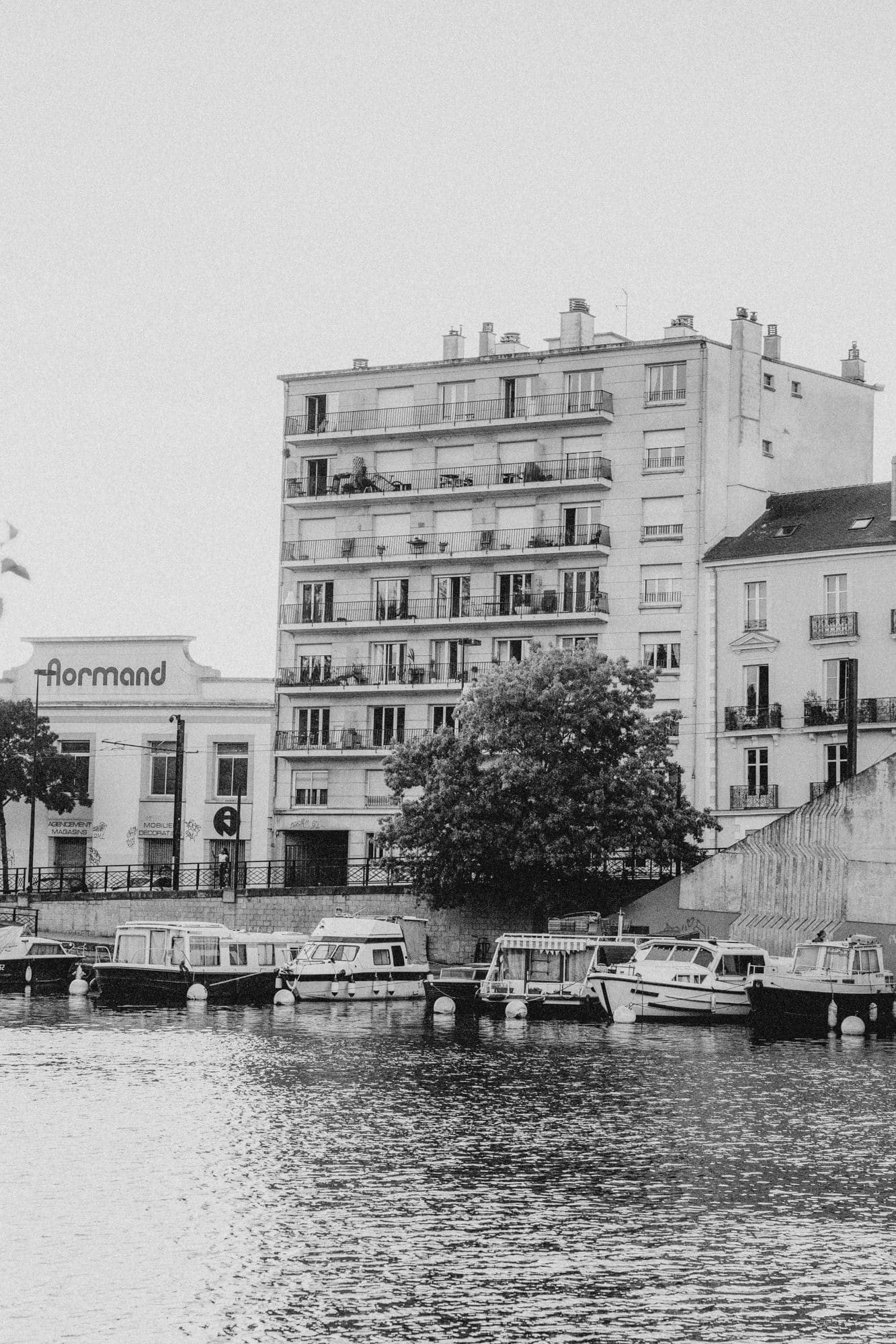 Black and white image of a residential building with balconies next to a marina with boats.